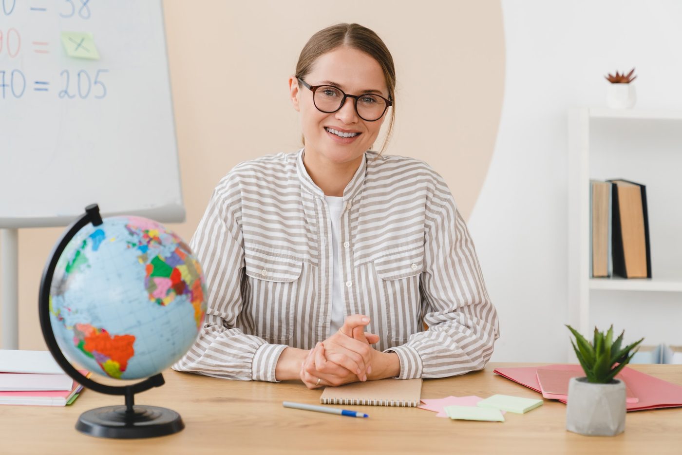 A teacher smiling at her desk beside a globe